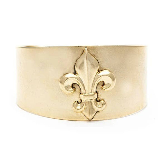 A gold-colored cuff bracelet featuring a Fleur-de-Lis design, displayed against a white background.