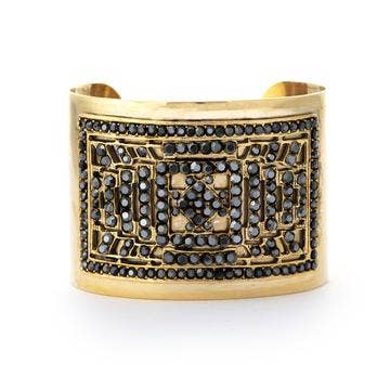 A gold-colored chunky bracelet adorned with intricate designs and detailed with swarovski crystals, displayed against a white background.
