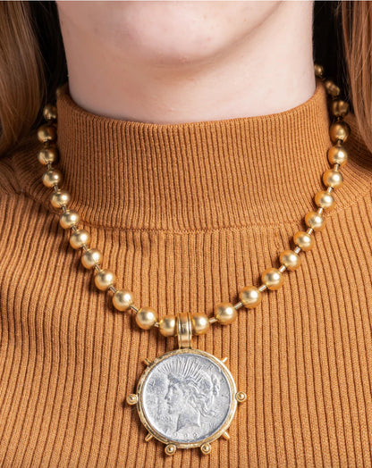 A person wearing a Roman coin necklace with a ball chain design, featuring a 22K gold plating over brass.